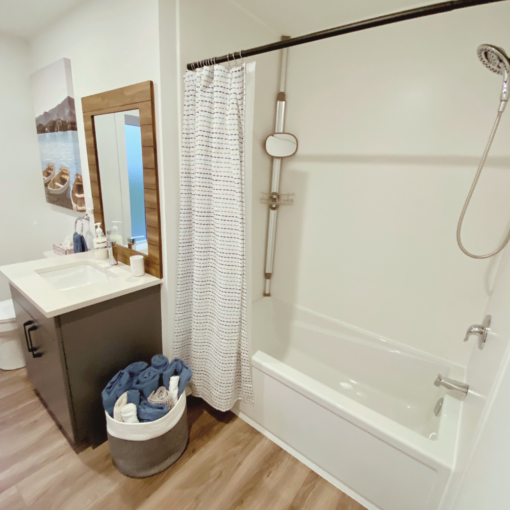 Modern bathroom with a white bathtub and shower combination featuring a curved curtain rod and adjustable shower head. A white and navy polka dot shower curtain is partially drawn.