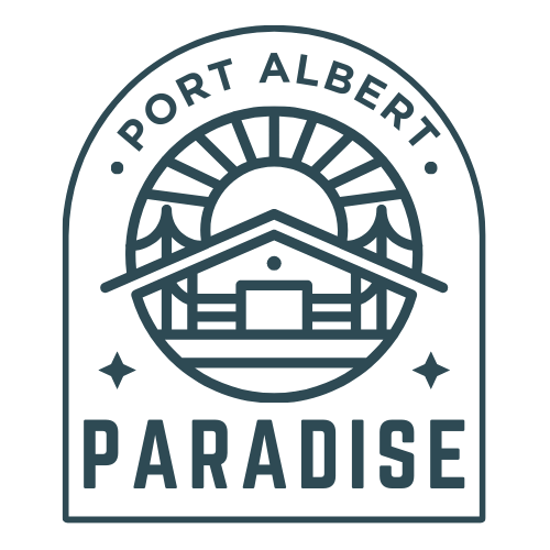 Logo for 'Port Albert Paradise' featuring a stylized cabin with a sun rising behind it, two curved bridge-like shapes on each side, and bold text below. The design is enclosed in an arched badge outline with decorative stars on each side of the word 'PARADISE.